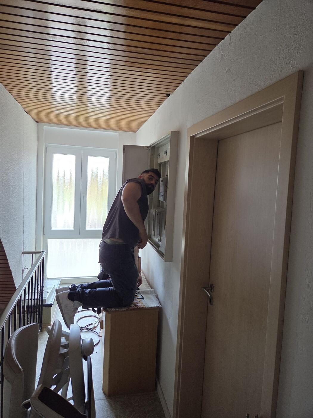 Monteur arbeitet an der geöffneten Unterverteilung im Hausflur, Zählerfeld und Sicherungsautomaten sichtbar