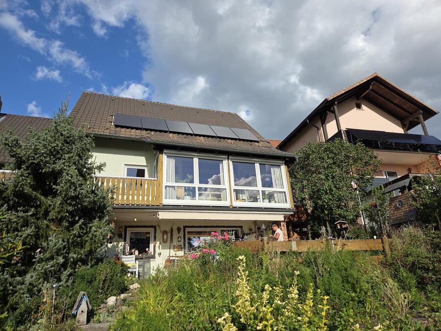 Sechs schwarze Solarmodule auf dem Dach eines Wohnhauses in Kueps, davor ein Garten