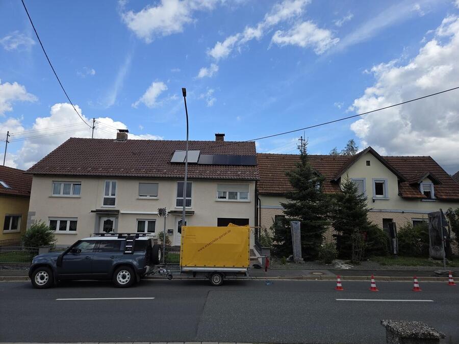 Vier schwarze Solarmodule auf dem Ziegeldach eines Wohnhauses in Marktrodach, davor der Montagewagen