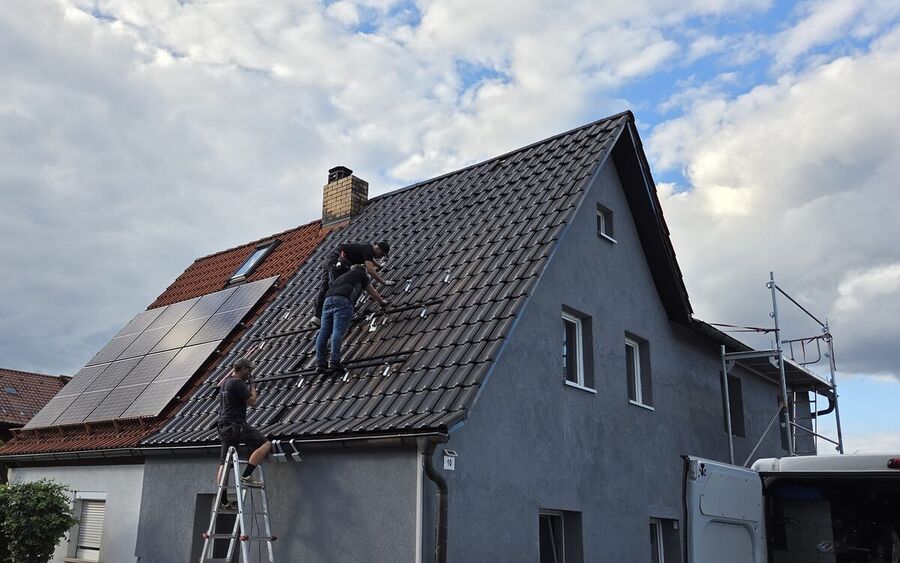 Drei Monteure auf dem Ziegeldach eines Wohnhauses in Kronach setzen Dachhaken und Montageschienen