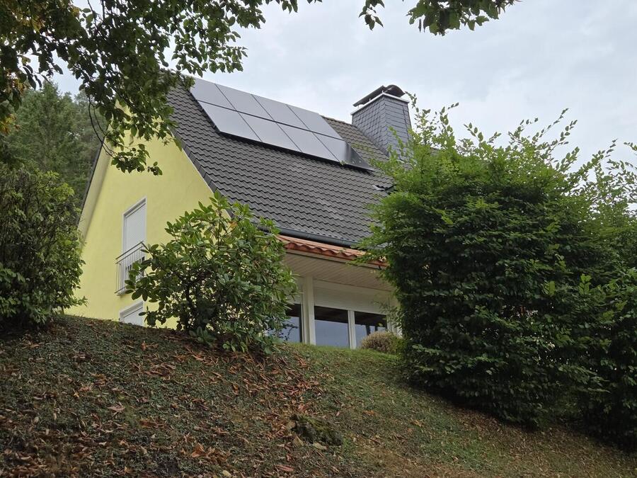 Acht schwarze Solarmodule auf dem Satteldach eines gelben Einfamilienhauses am Waldrand im Landkreis Kronach