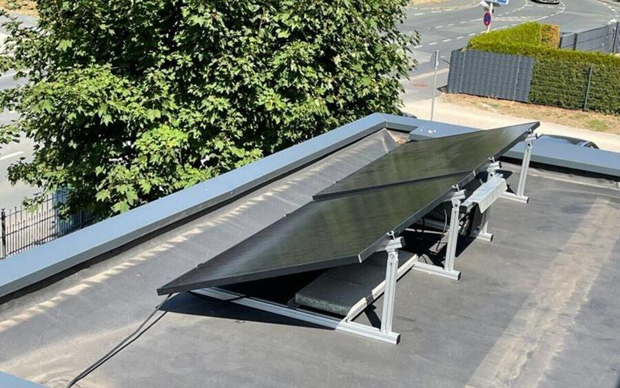 Zwei aufgeständerte Solarmodule auf einem Flachdach, dahinter Ortsdurchfahrt und Bäume