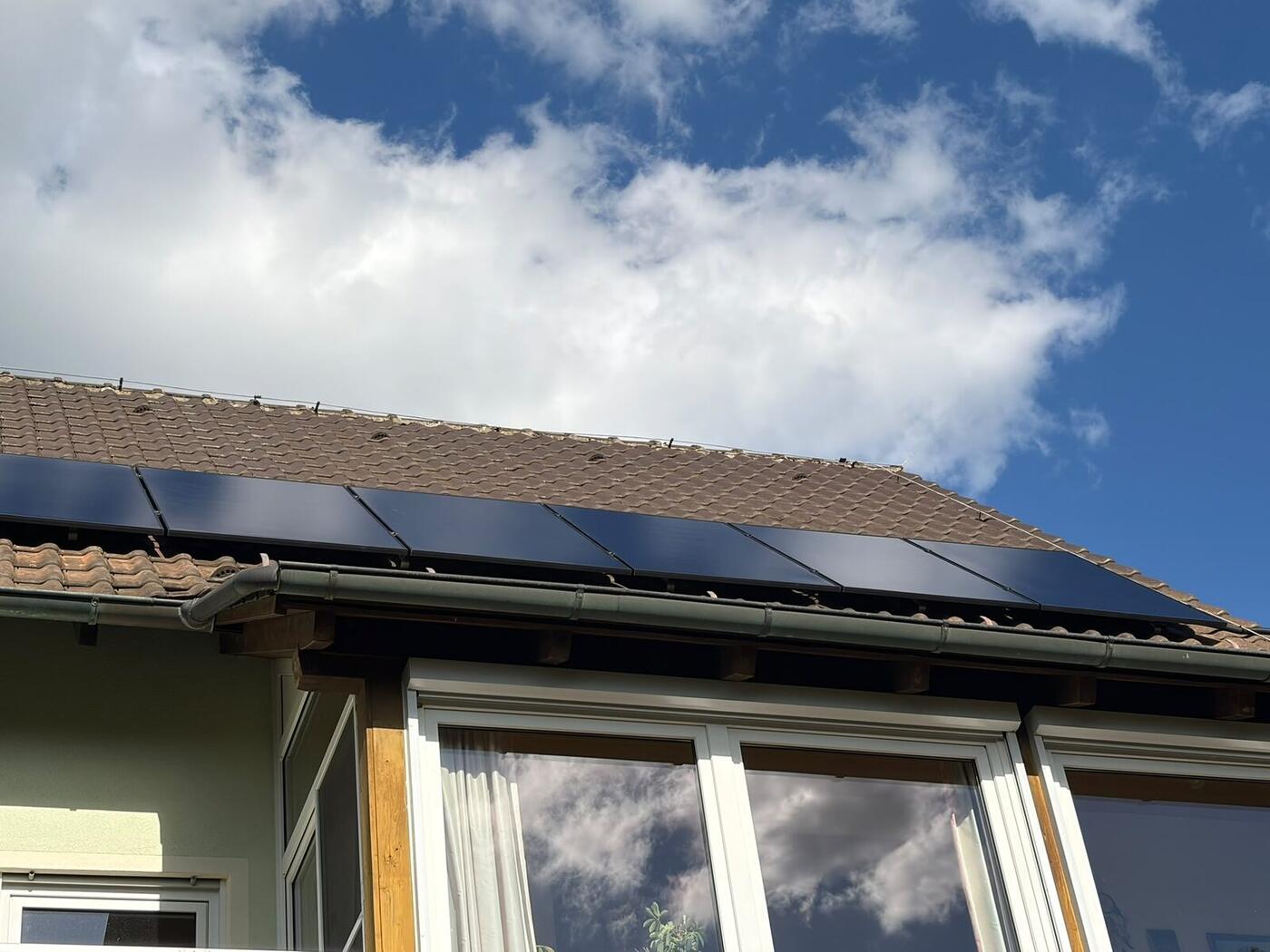Reihe schwarzer Solarmodule an der Traufe eines Ziegeldachs in Küps, dahinter blauer Himmel