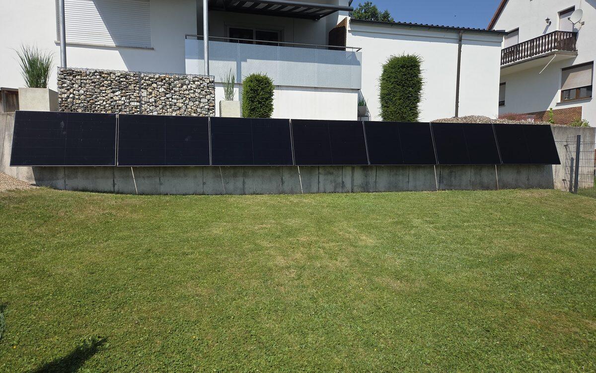 Reihe schwarzer Solarmodule an einer Betonmauer im Garten eines Wohnhauses in Stockheim