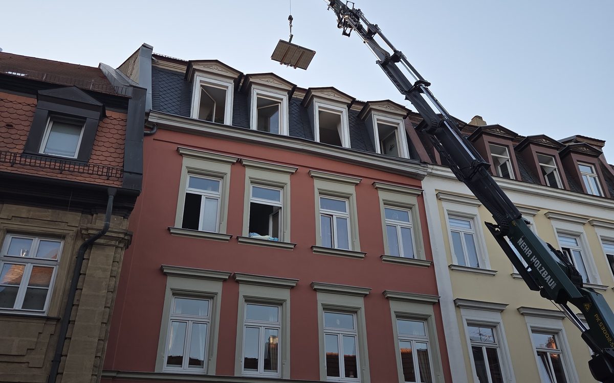 Kran hebt Material für eine Photovoltaik-Dachanlage auf ein Mehrfamilienhaus in der denkmalgeschützten Bamberger Altstadt