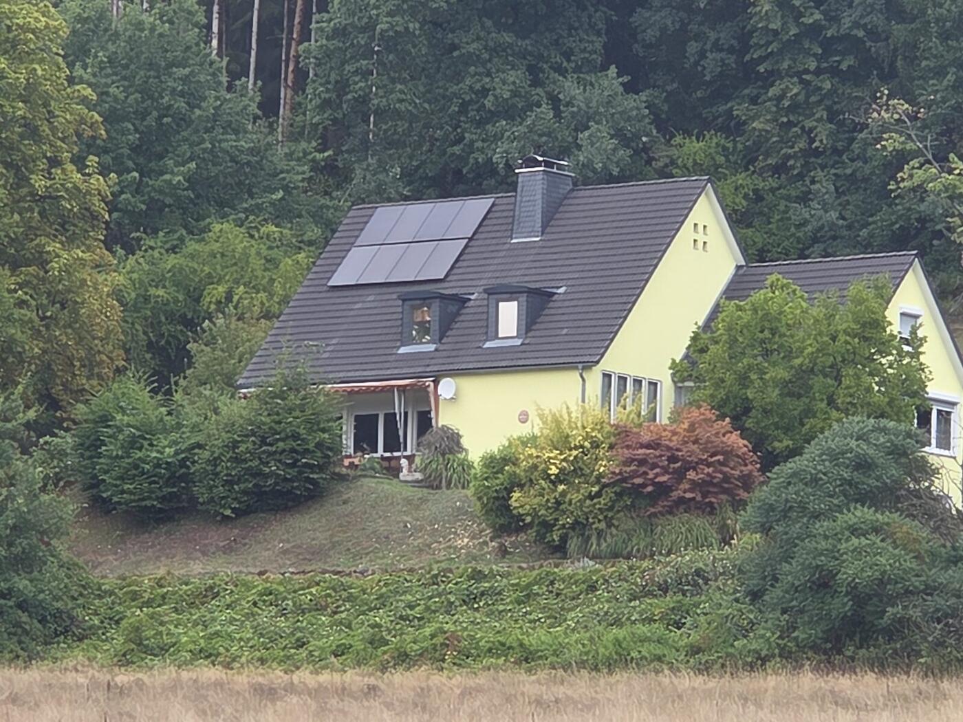 Freistehendes gelbes Einfamilienhaus am Waldrand im Landkreis Kronach, auf dem Satteldach liegen Solarmodule