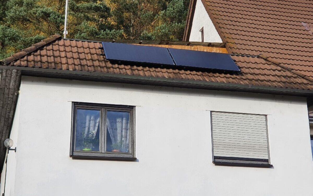 Zwei grossflächige Solarmodule in der Ziegelfläche eines Satteldachs, dahinter Nadelwald