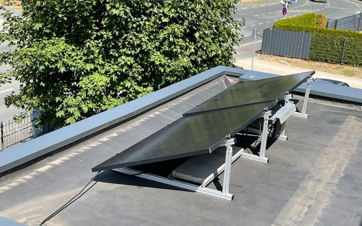 Zwei aufgeständerte Solarmodule auf einem Flachdach, dahinter Ortsdurchfahrt und Bäume