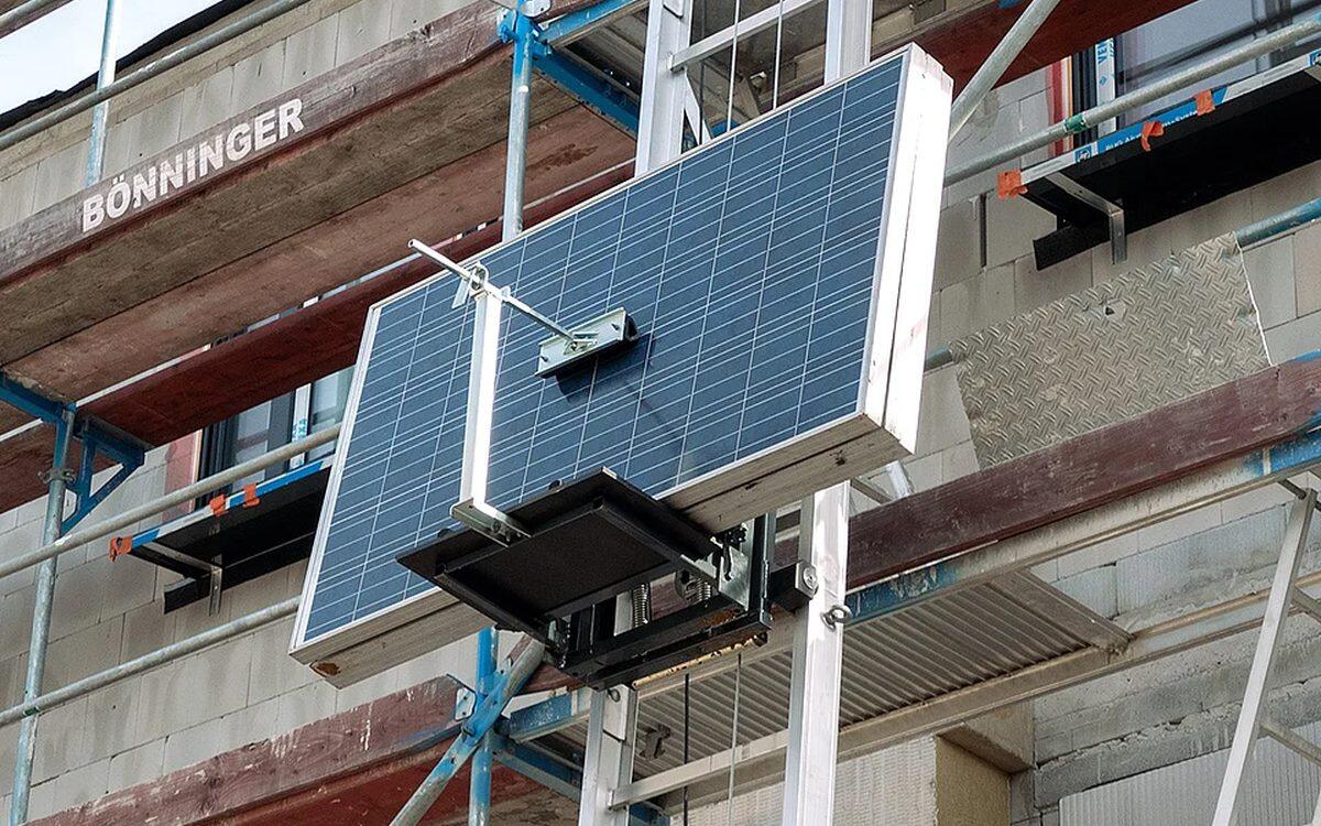 Bauaufzug an einem Baugerüst, auf der Transportpritsche liegt ein Solarmodul
