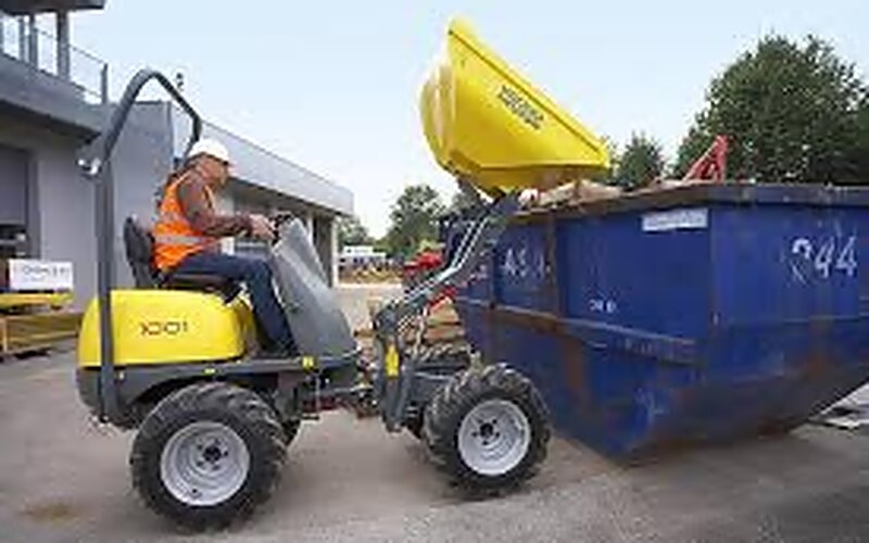 Dumper von Wacker Neuson kippt seine Mulde über Kopf in einen blauen Bauschuttcontainer, der Fahrer sitzt am Steuer